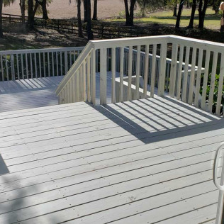 Freshly painted white deck with matching white railings featuring vertical balusters, overlooking a tree-lined yard