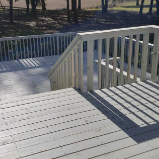 Corner section of white painted deck showing built-in seating area with white railings and tree views