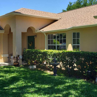 Freshly painted single-story home exterior in beige/tan with white trim, arched entryway, and manicured landscaping