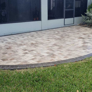 Multi-colored paver patio or driveway with basketweave pattern in tan and brown tones adjacent to screened enclosure