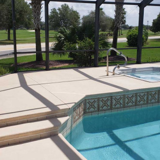 Tan-painted concrete pool deck surrounding inground pool with decorative tile border inside screened enclosure