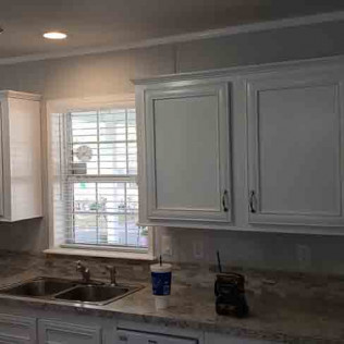 Freshly painted white kitchen cabinets with raised panel doors, dark hardware, and gray walls with granite countertops