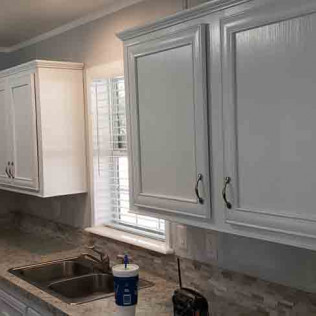 White painted kitchen cabinets featuring traditional raised panel design with oil-rubbed bronze hardware and window above sink