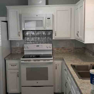 Complete white painted kitchen cabinet makeover with decorative tin backsplash, white appliances, and granite countertops