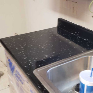 Black epoxy countertop with white speckled pattern in progress, showing glossy finish near sink area with protective masking
