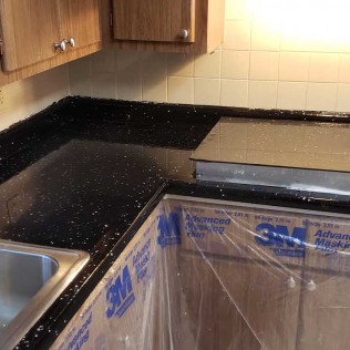 L-shaped black epoxy countertop with starry white speckle effect and high-gloss reflective finish, cabinets protected with plastic