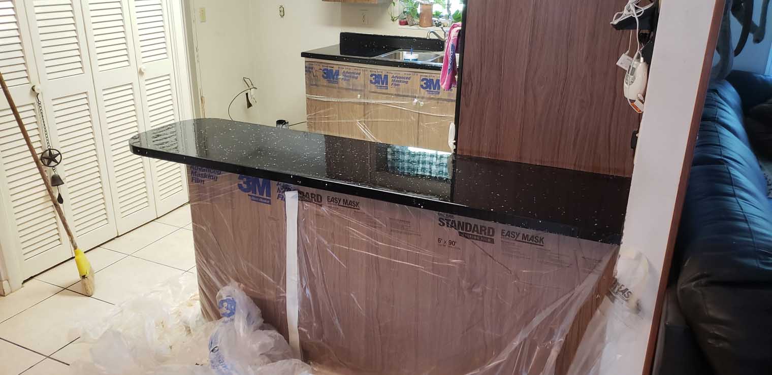 Completed black epoxy countertop installation with white speckled design on kitchen island and perimeter counters, cabinets masked during application