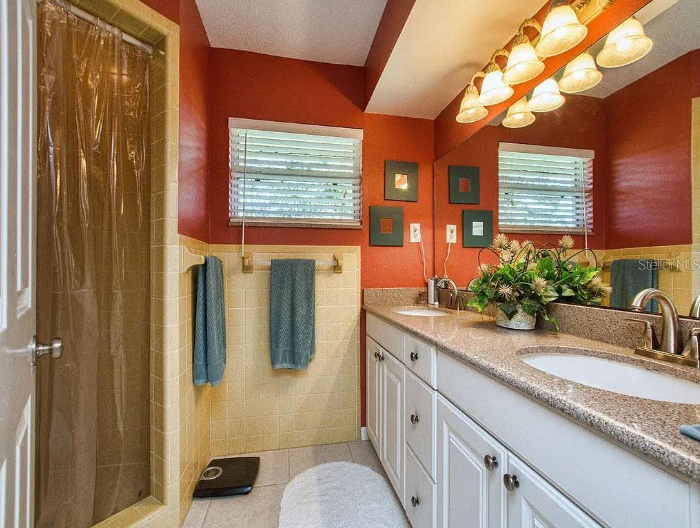 Bathroom interior with burnt orange painted walls, beige tile wainscoting, white vanity cabinet and granite countertop with decorative lighting