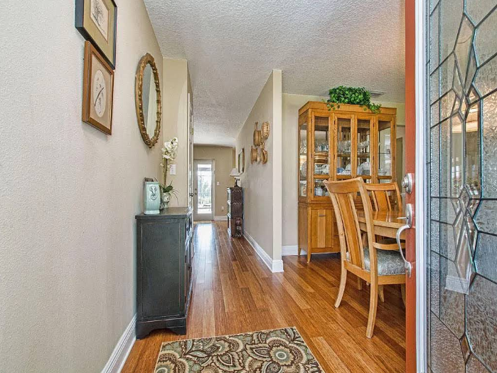 Long hallway with light beige painted walls, wood flooring, wall decor and view into dining room with wood furniture