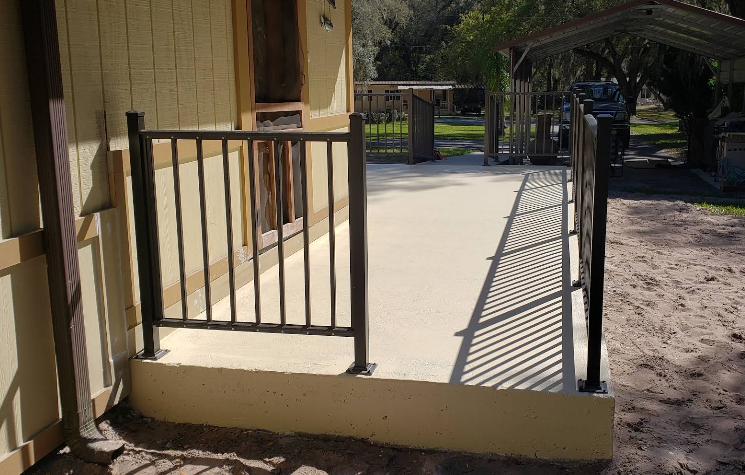 Painted concrete porch with black metal railing and beige non-slip surface at home entrance