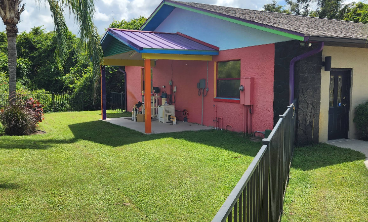 Home exterior with pink painted stucco walls, colorful accent trim in blue, purple and orange with covered patio