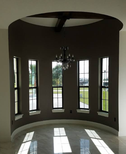 Curved interior room with dark gray painted walls, white trim windows and elegant chandelier in center
