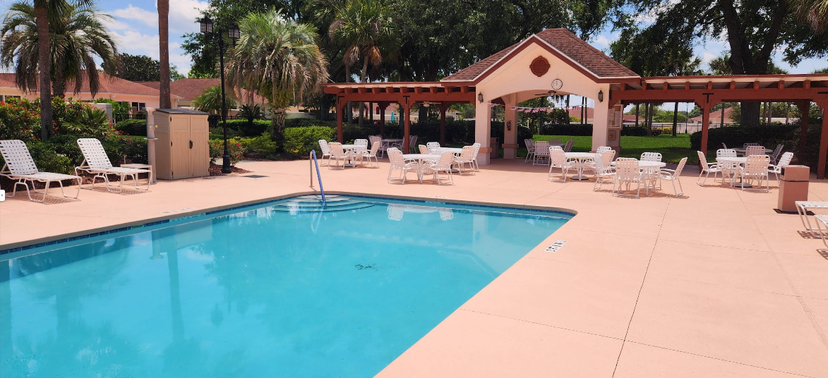 Community pool area with peachy-tan painted concrete deck and covered pavilion seating area