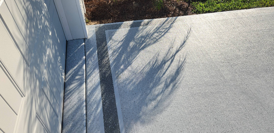 Gray painted concrete driveway with decorative border pattern next to white home exterior