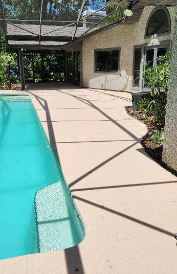 Residential pool with light tan painted concrete deck and screened enclosure beside stucco home