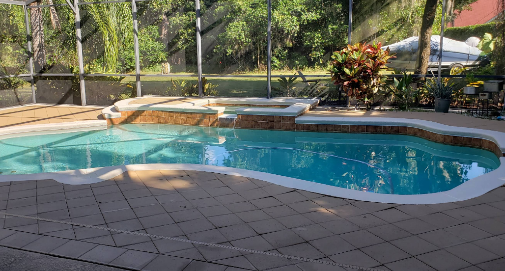 Freeform pool with decorative tile trim and gray paver deck under screened enclosure