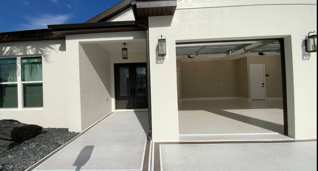 Light gray painted concrete driveway in front of beige home with white garage door