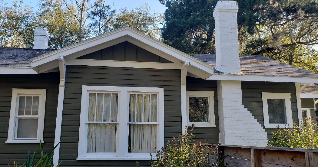 Residential home exterior painted in dark gray with white trim and painted brick chimney