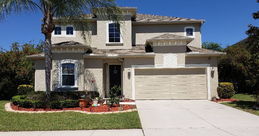 Two-story stucco home painted in beige with white painted concrete driveway and landscaped front yard