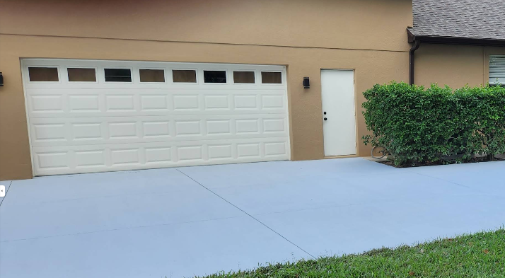 Light gray painted concrete driveway in front of beige home with white garage door