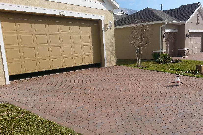 Red brick paver driveway in front of beige stucco home with painted garage door
