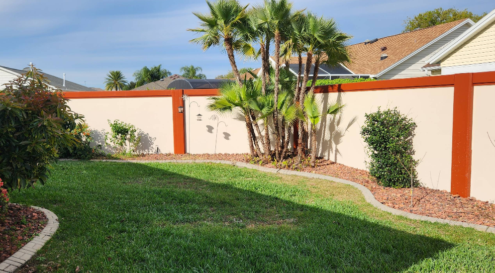Residential privacy fence painted two-tone orange and beige with palm tree cluster and mulched landscaping