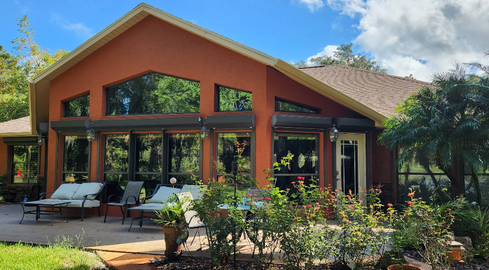 Large home exterior painted in rust red with expansive windows and screened patio overlooking landscaped yard