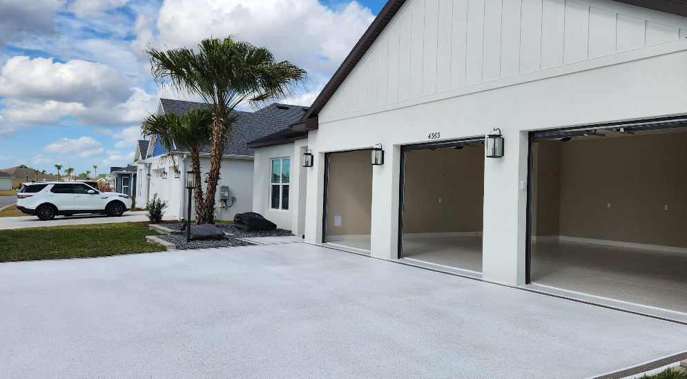 Modern white home with three-car garage featuring light gray epoxy flooring and matching painted driveway