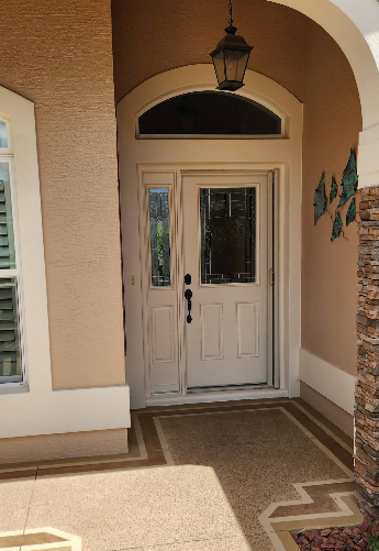 Covered home entrance with speckled tan concrete painted porch and white door with sidelights