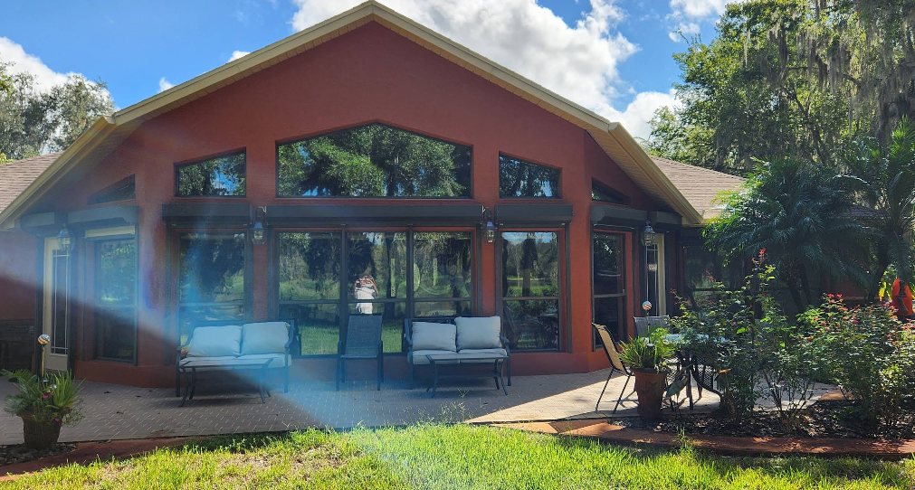 Home exterior painted in terracotta red with large screened patio and windows overlooking landscaped yard