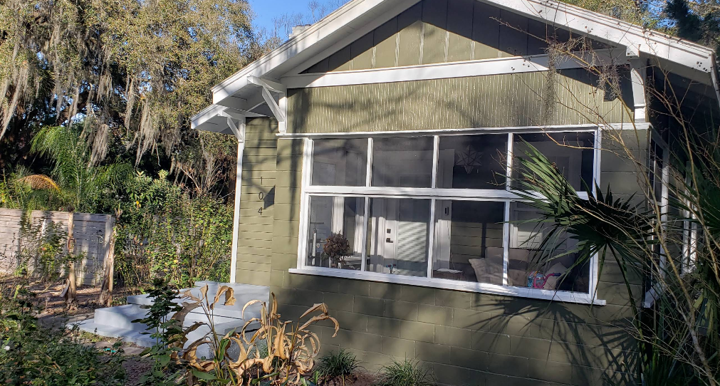 Cottage exterior painted in sage green with white trim and screened windows under moss-draped trees