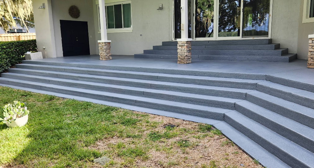 Wide gray painted concrete steps and platform leading to home entrance with stone pillar accents