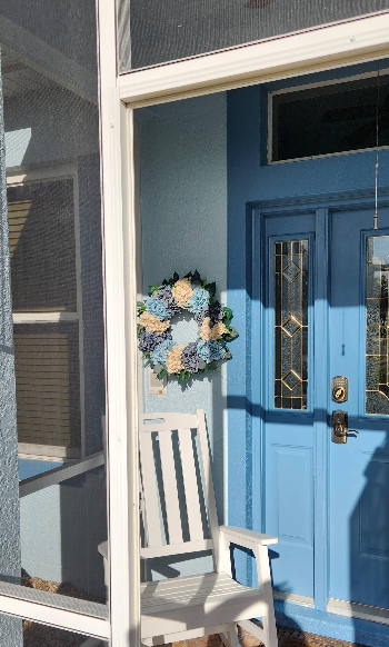 Home entrance painted in coordinating blue tones with decorative wreath and white rocking chair