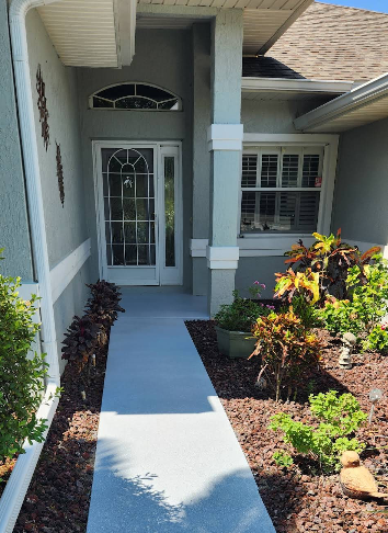 Light blue painted concrete walkway leading to home entrance with decorative landscaping and mulch beds
