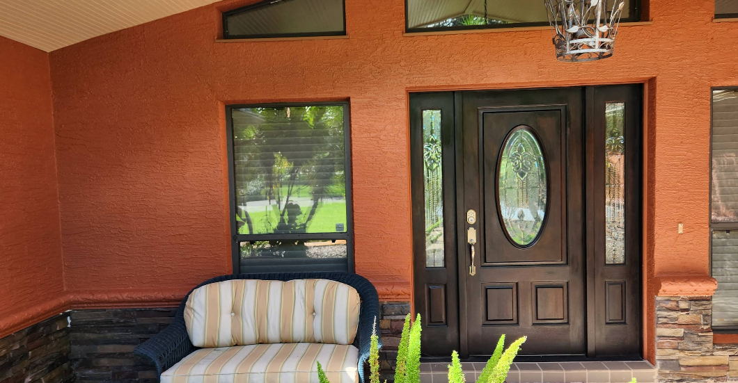 Covered porch entrance painted rust orange with dark wood door, sidelights and wicker seating