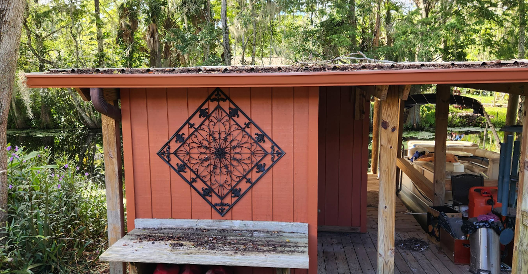 Outdoor storage shed painted in terracotta red with decorative metal accent and natural wood posts