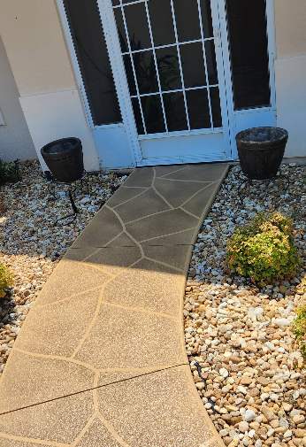 Decorative painted concrete walkway with flagstone pattern in gray and tan tones through pebble landscaping