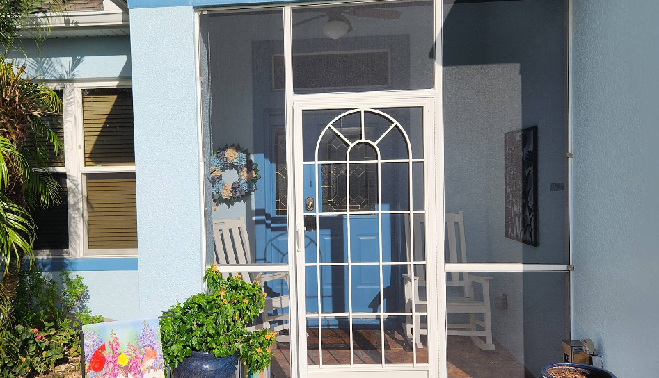 Light blue painted home entrance with white decorative screen door and wreath surrounded by plants