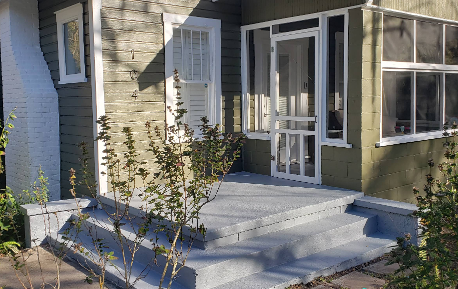 Light gray speckled painted concrete steps and porch at sage green painted home with white screen door