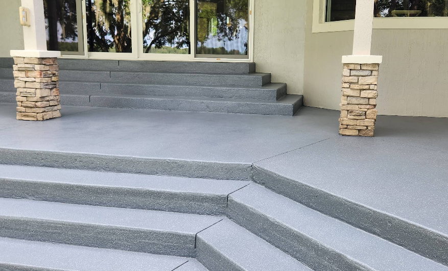 Wide gray painted concrete steps with stone pillar accents leading to covered porch entrance