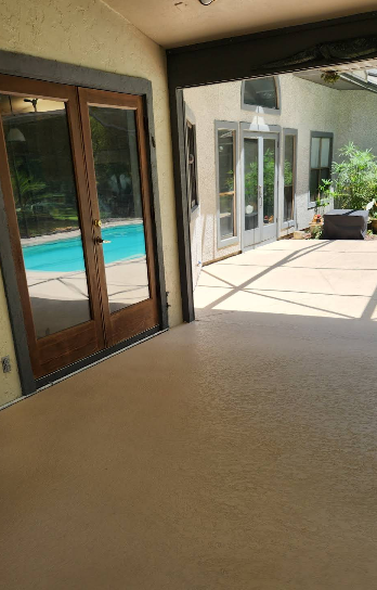Covered patio with light beige painted concrete floor overlooking pool area with glass doors