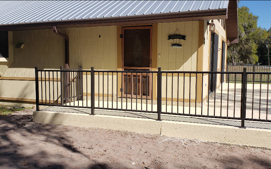 Pale yellow painted home with light beige painted concrete porch and wheelchair ramp with black metal railing
