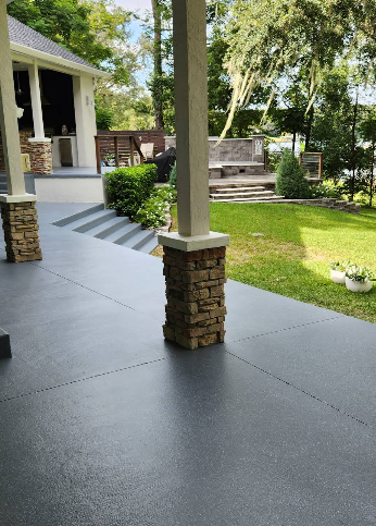Covered porch with dark gray painted concrete floor, white stone pillars and steps overlooking lakefront